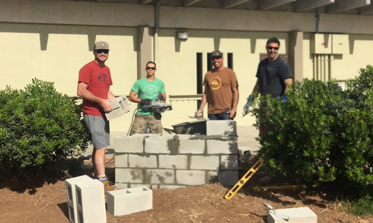 Four volunteers stand behind a partially built concrete-block spirit wall