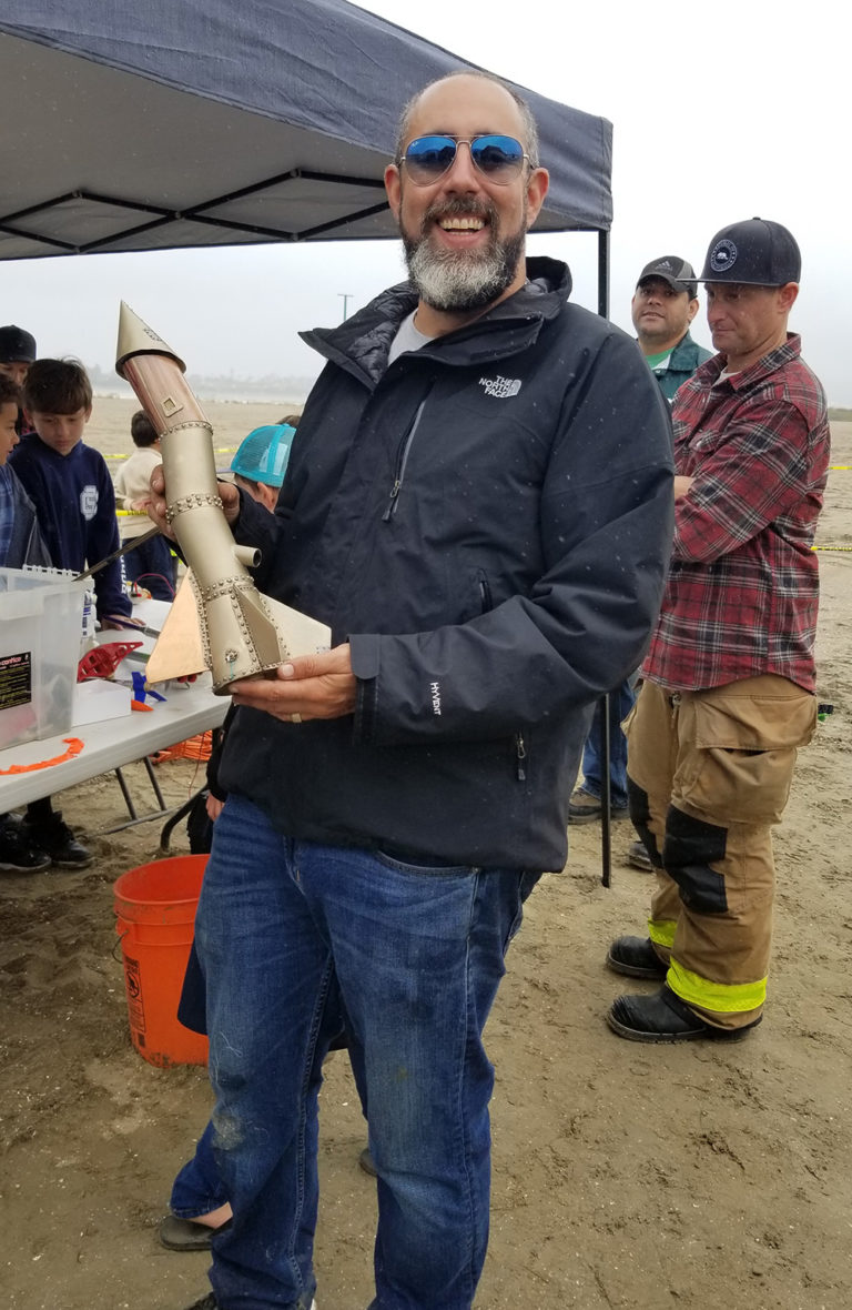 An adult holding a model rocket beneath an outdoor canopy